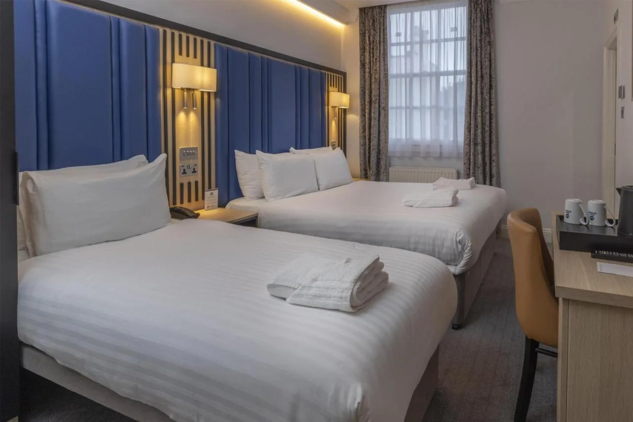 a hotel room with two beds and a desk at Best Western Victoria Palace in London